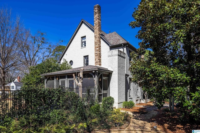 view of side of property featuring brick siding, a chimney, and fence