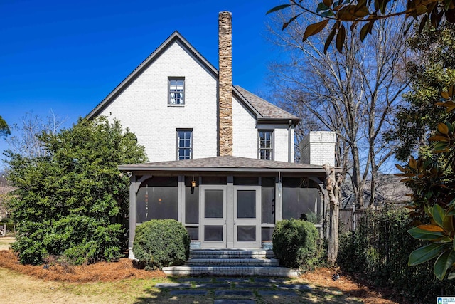 view of front facade featuring brick siding, a shingled roof, entry steps, a chimney, and a sunroom