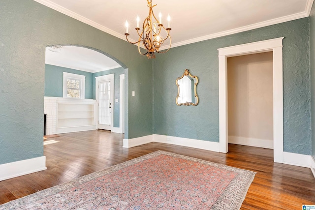 unfurnished room featuring a chandelier, wood finished floors, ornamental molding, a textured wall, and arched walkways