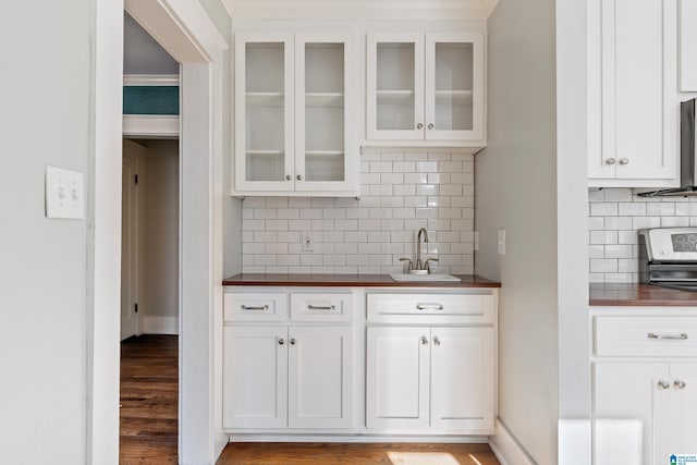 kitchen with a sink, glass insert cabinets, wood finished floors, and white cabinetry