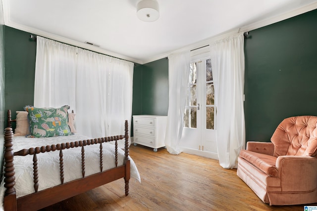 bedroom with french doors, visible vents, wood finished floors, and crown molding