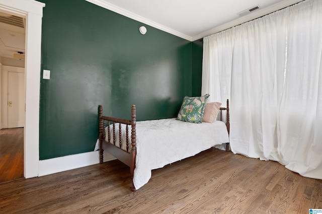 bedroom featuring baseboards, wood finished floors, visible vents, and ornamental molding