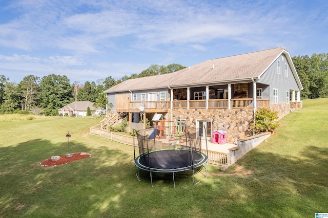 rear view of property with stone siding, a trampoline, a playground, a yard, and a shingled roof