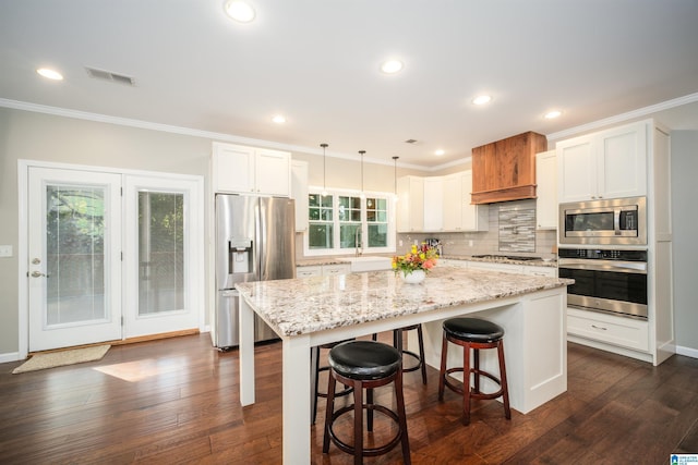 kitchen featuring backsplash, appliances with stainless steel finishes, a kitchen island, and ornamental molding