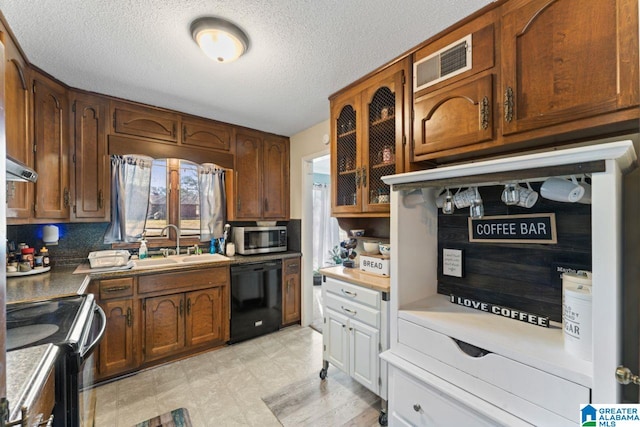 kitchen with visible vents, black appliances, a sink, glass insert cabinets, and light floors