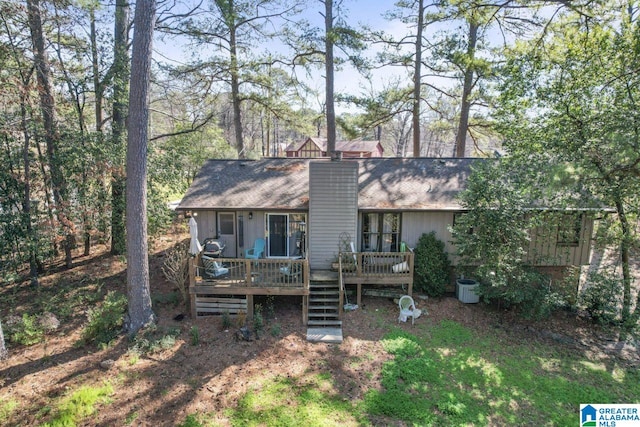 back of house with a chimney, a deck, and roof with shingles