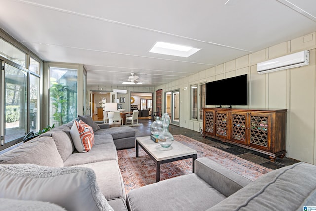 living room featuring a wall unit AC, a skylight, and a ceiling fan