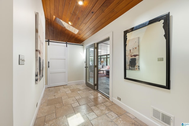 hallway featuring visible vents, baseboards, a barn door, wooden ceiling, and stone tile flooring