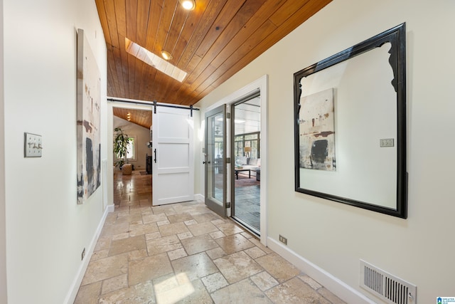 hall featuring visible vents, stone tile floors, a barn door, baseboards, and wood ceiling