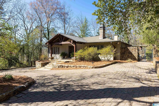 rear view of house with board and batten siding, a chimney, decorative driveway, and a gate