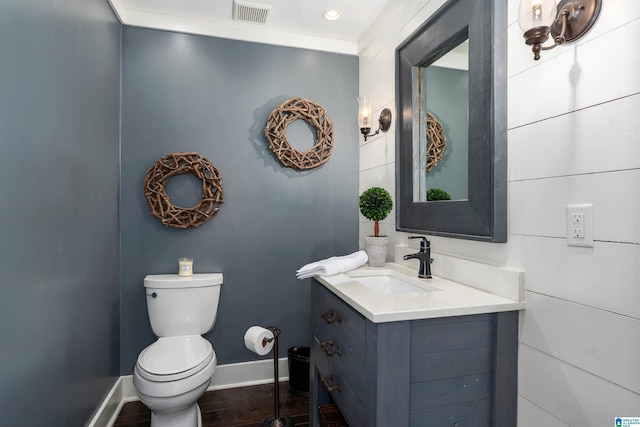 half bath with visible vents, toilet, wood finished floors, baseboards, and vanity