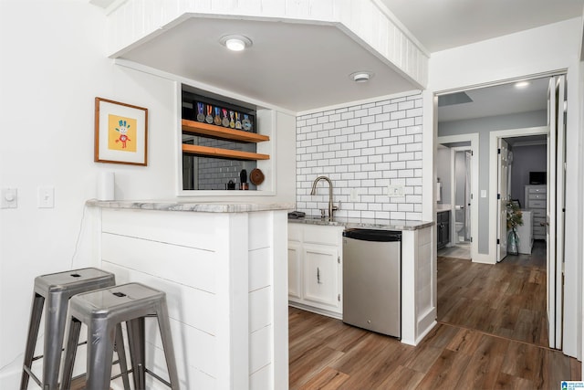 kitchen with wood finished floors, a sink, decorative backsplash, white cabinets, and dishwasher