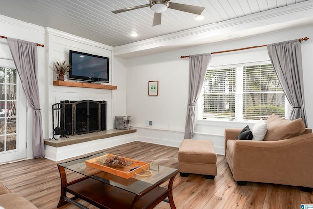 living area with a fireplace with raised hearth, wood ceiling, wood finished floors, and a ceiling fan