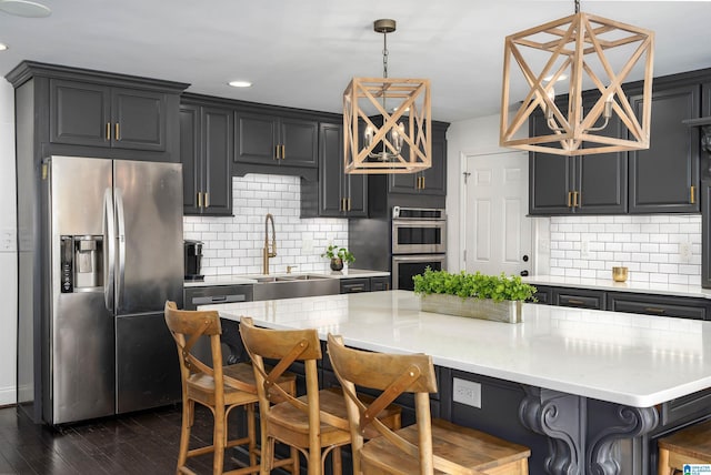 kitchen with backsplash, dark wood finished floors, a breakfast bar, appliances with stainless steel finishes, and a sink