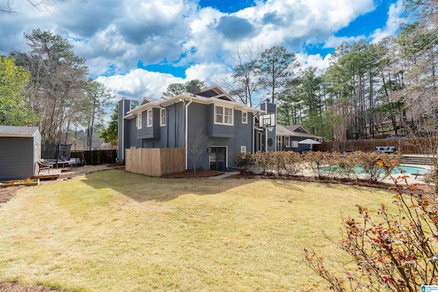 back of house with a pool, fence, a yard, a chimney, and a trampoline