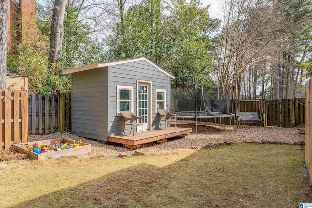 view of outdoor structure with an outbuilding, a fenced backyard, and a trampoline