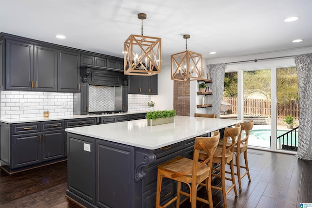 kitchen featuring backsplash, a center island, a chandelier, light countertops, and dark wood-style flooring