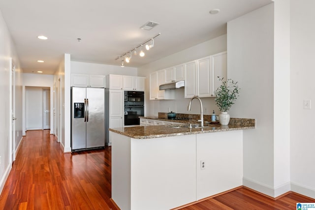 kitchen featuring dobule oven black, a sink, under cabinet range hood, dark stone counters, and stainless steel fridge with ice dispenser