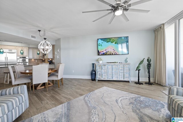 living area with ceiling fan with notable chandelier, light wood-style flooring, baseboards, and visible vents