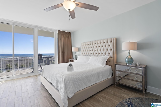 bedroom with ceiling fan, a water view, floor to ceiling windows, wood finished floors, and access to outside