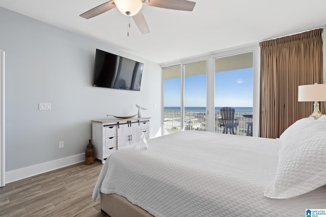 bedroom with ceiling fan, baseboards, a wall of windows, wood finished floors, and access to outside