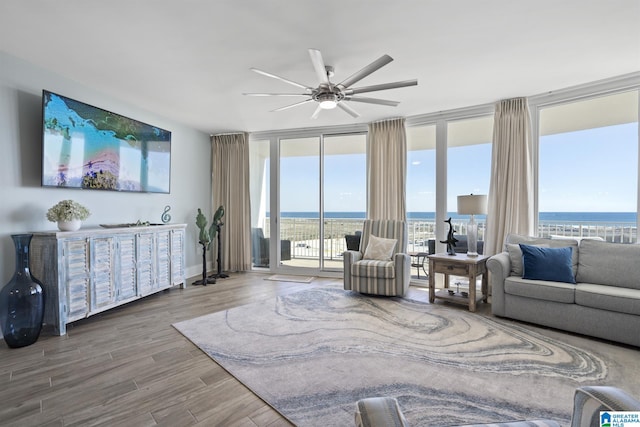 living room with ceiling fan, a wall of windows, a water view, and wood finished floors