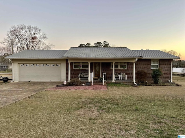 ranch-style home with an attached garage, covered porch, concrete driveway, brick siding, and metal roof