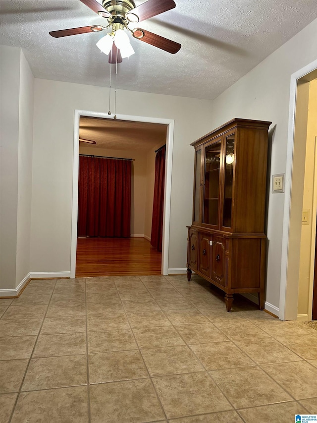 hallway with light tile patterned floors, baseboards, and a textured ceiling