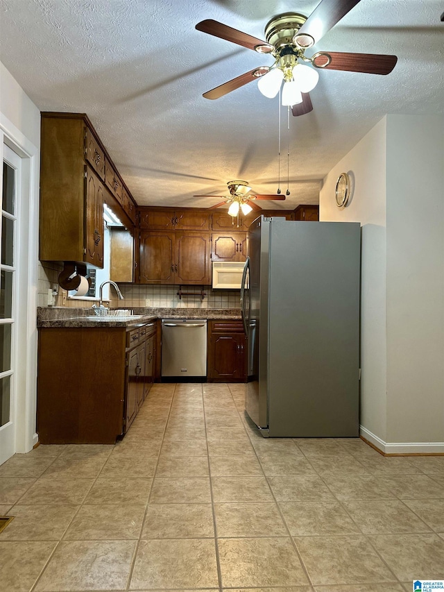 kitchen with a sink, backsplash, dark countertops, a textured ceiling, and appliances with stainless steel finishes