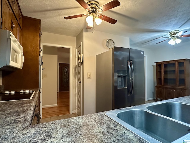 kitchen featuring white microwave, black electric stovetop, stainless steel fridge with ice dispenser, a textured ceiling, and a sink