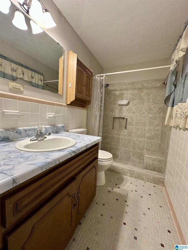 full bath featuring toilet, a textured ceiling, a tile shower, tile walls, and vanity