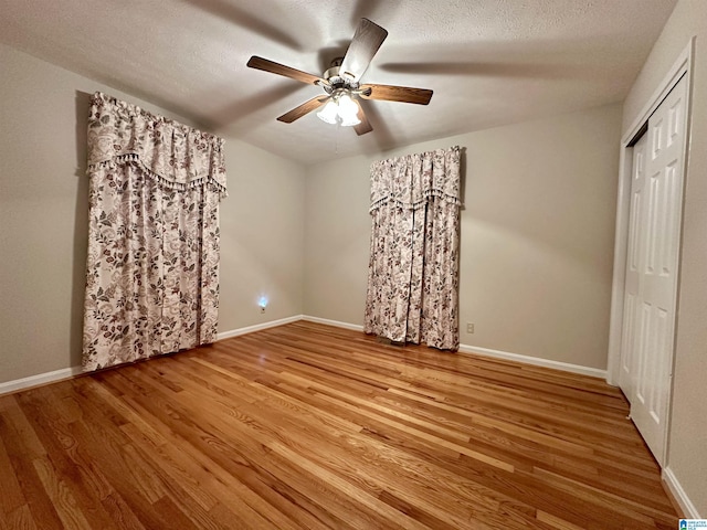 unfurnished bedroom with a closet, a textured ceiling, baseboards, and wood finished floors