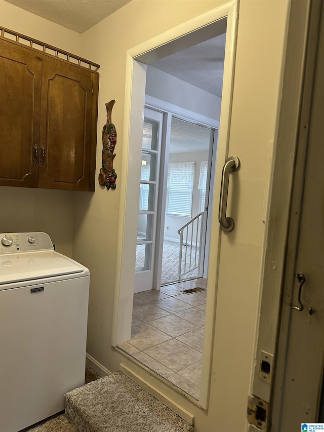 clothes washing area with light tile patterned floors, cabinet space, a textured ceiling, and washer / dryer