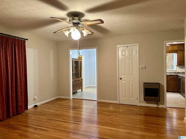 spare room with baseboards, heating unit, light wood-style floors, and ceiling fan