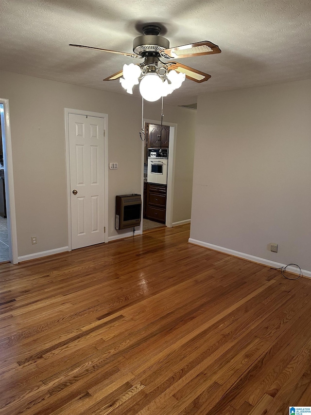 unfurnished living room with baseboards, wood finished floors, heating unit, a textured ceiling, and a ceiling fan