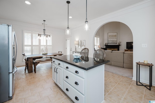 kitchen featuring a center island, white cabinetry, freestanding refrigerator, arched walkways, and crown molding