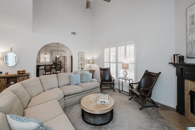 tiled living area with arched walkways, visible vents, a fireplace, and a towering ceiling