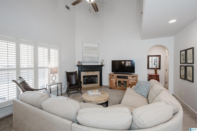 living area with visible vents, a high ceiling, arched walkways, a tiled fireplace, and carpet flooring