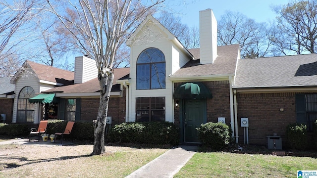 view of front of house with brick siding, a chimney, a front lawn, and roof with shingles