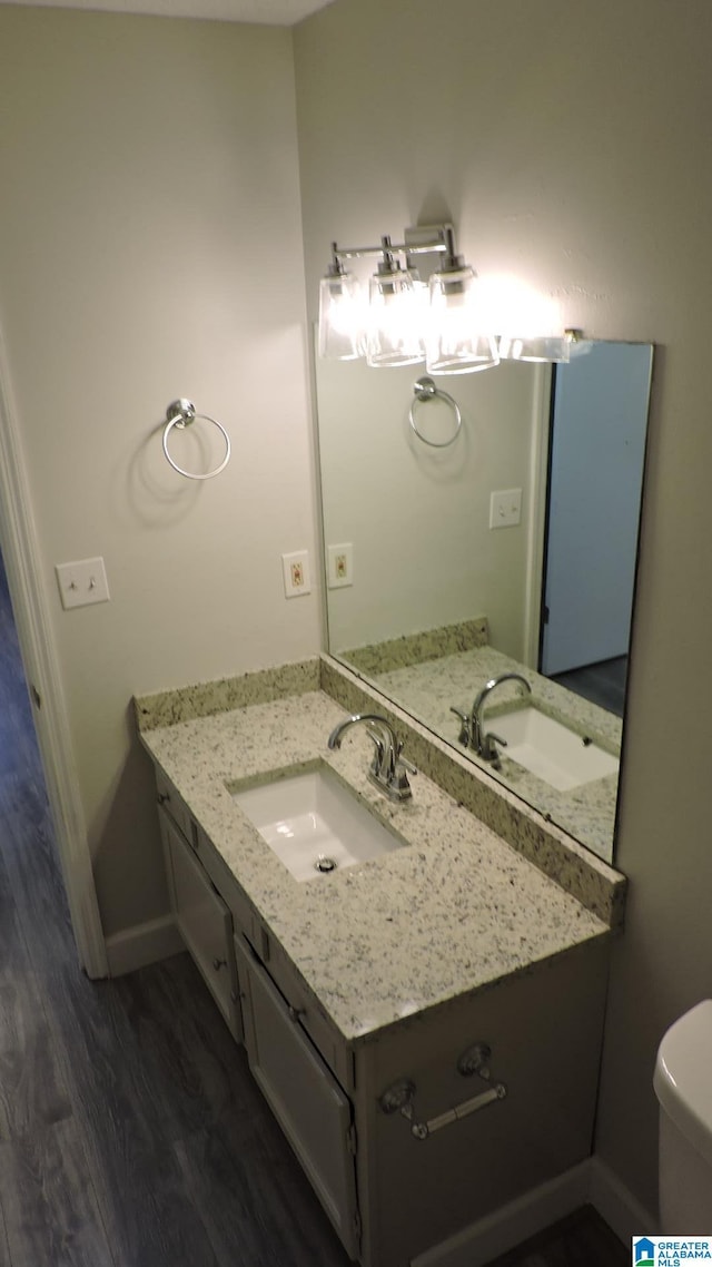 half bath featuring vanity, toilet, wood finished floors, and baseboards