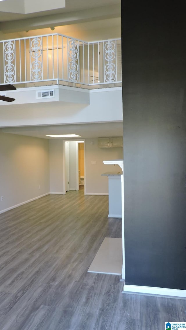 unfurnished living room with visible vents, baseboards, a towering ceiling, wood finished floors, and a ceiling fan