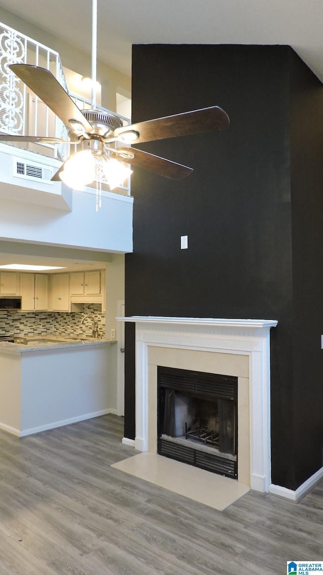room details featuring wood finished floors, visible vents, a fireplace with flush hearth, ceiling fan, and backsplash