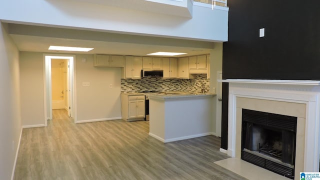 kitchen featuring light wood-type flooring, stainless steel microwave, a fireplace with flush hearth, and tasteful backsplash