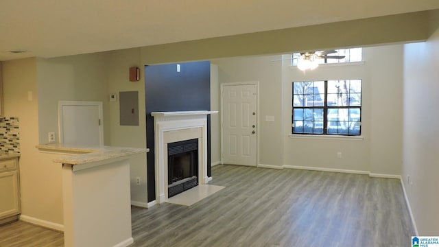 unfurnished living room with a ceiling fan, baseboards, light wood finished floors, electric panel, and a fireplace with flush hearth