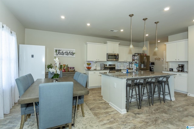 kitchen with a center island with sink, a kitchen bar, light stone counters, decorative backsplash, and stainless steel appliances