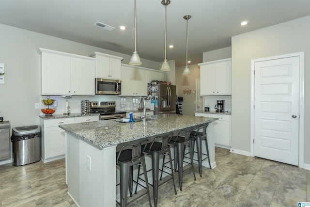 kitchen featuring visible vents, a center island with sink, a sink, stainless steel appliances, and decorative backsplash