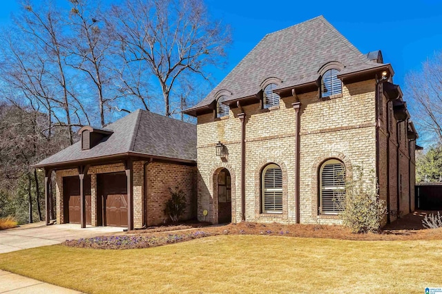 french country style house with driveway, a shingled roof, a front lawn, a garage, and brick siding