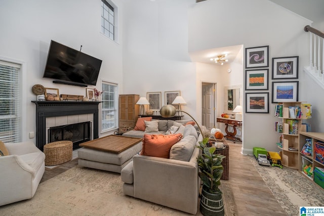 living area with a tiled fireplace, stairway, a towering ceiling, and wood finished floors