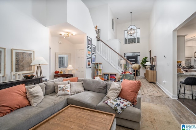 living area with stairway, a high ceiling, an inviting chandelier, light wood finished floors, and baseboards