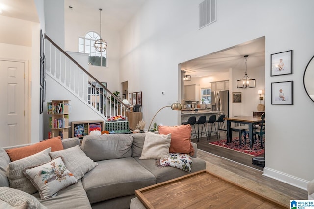 living area featuring visible vents, stairway, an inviting chandelier, and wood finished floors